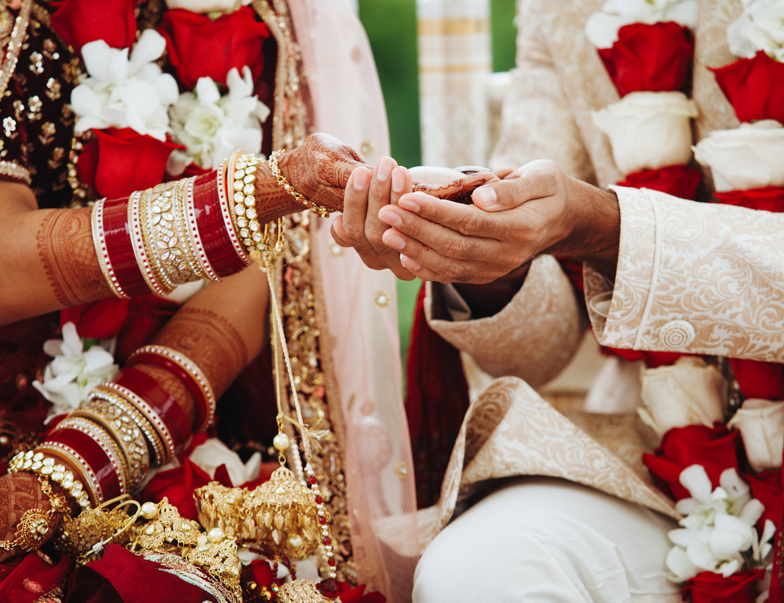 Close-up of bride and groom’s hands during a Hindu wedding ceremony, with the bride’s henna-adorned hands and red bangles over the groom’s cupped palms, symbolizing sacred wedding rituals